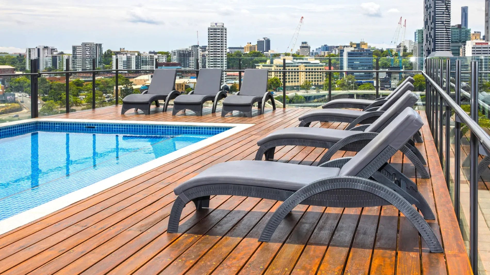 Gray lounge chairs on a wooden deck by a pool with a city skyline in the background